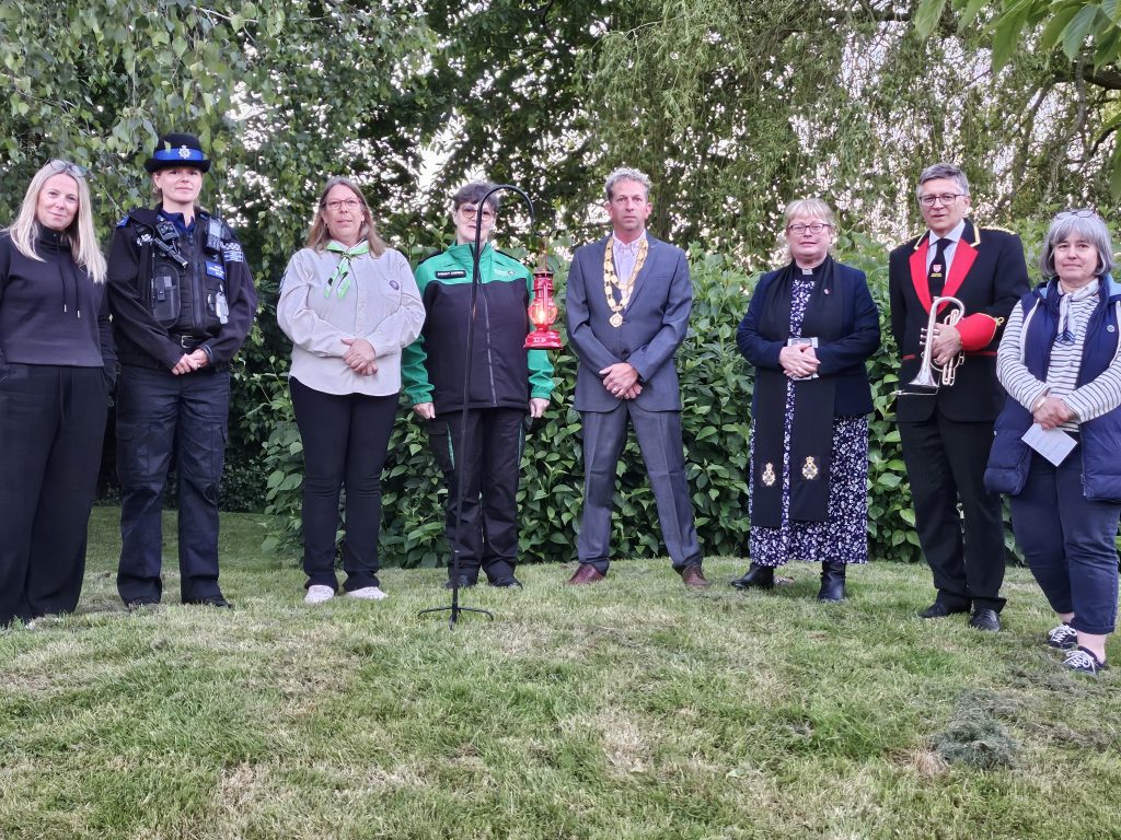 8 people stood around a red lamplight which is staked into the grass