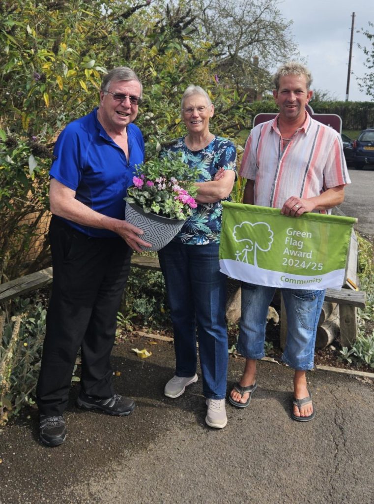 Three people stood outside by an office, one is holding a flowering planter.